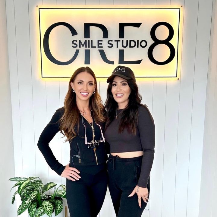 Two women posing in front of a lit “CR8 Smile Studio” sign.