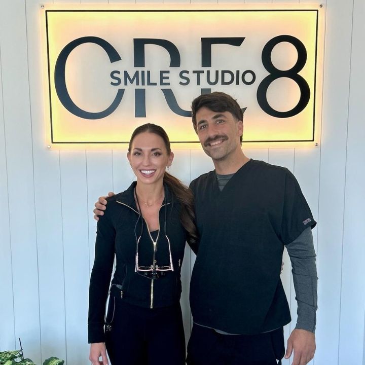 Two people posing in front of a glowing OR8 Smile Studio sign.