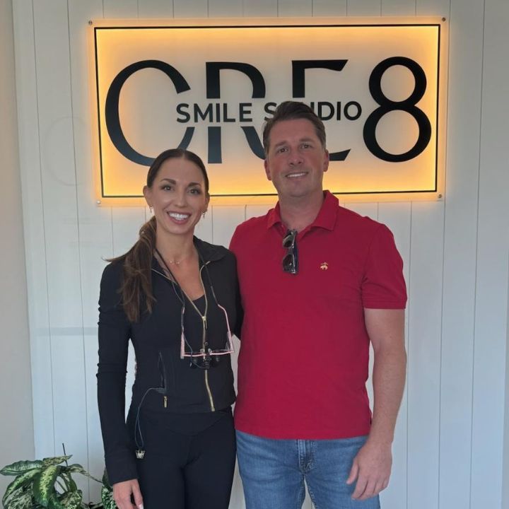 Two people standing in front of a lit CRE8 Smile Studio sign, smiling indoors.