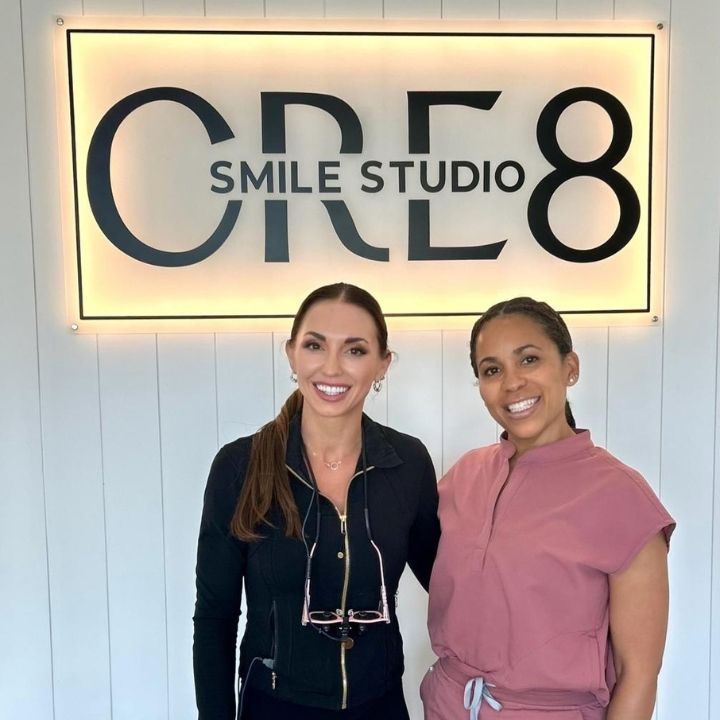 Two smiling people standing in front of a lit “CRE8 Smile Studio” sign