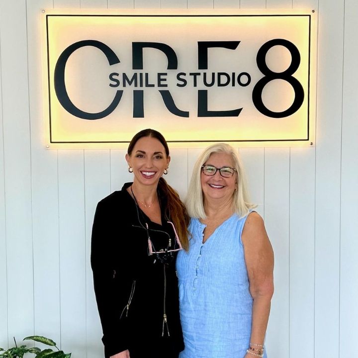 Two women standing smiling in front of a CBO Smile Studio sign