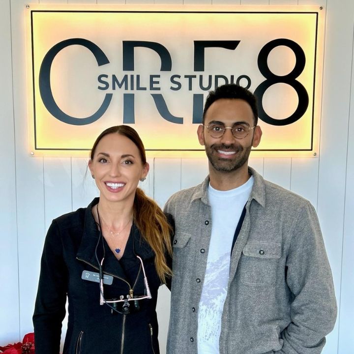 Two smiling people standing in front of a CRE8 Smile Studio sign.