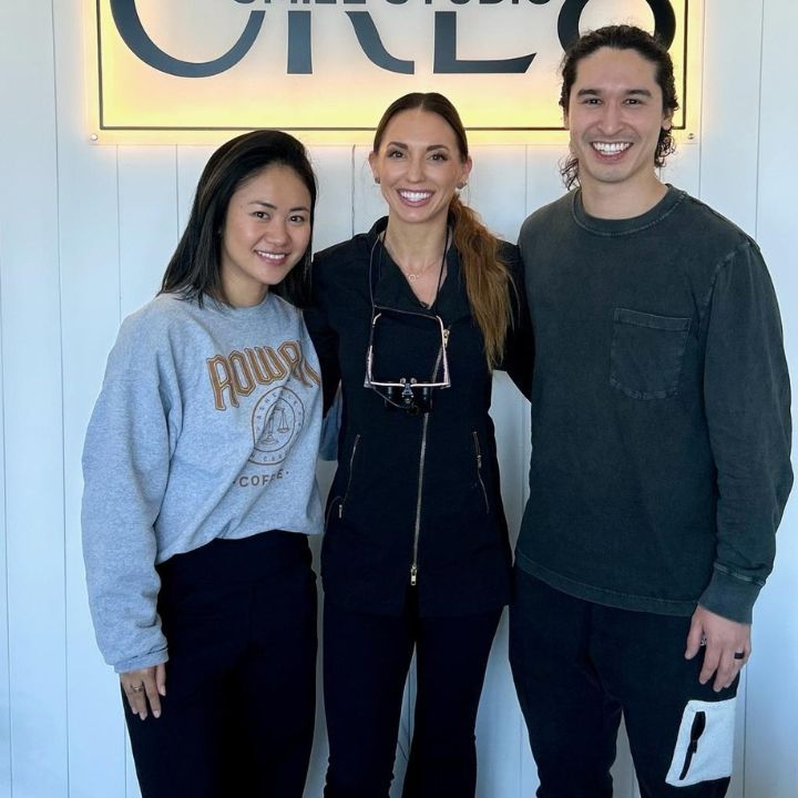Three smiling people posing indoors in front of a lit sign.