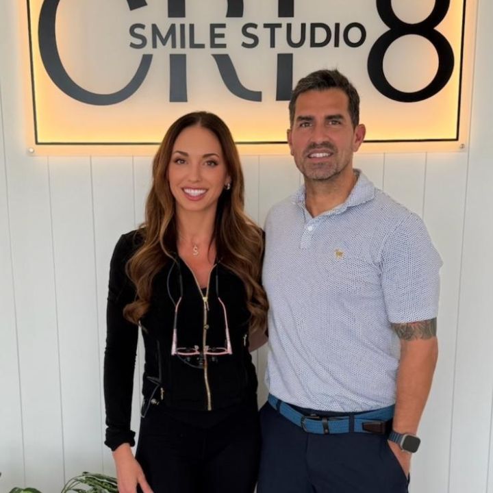 Two people smiling in front of a “Smile Studio” sign, standing indoors.