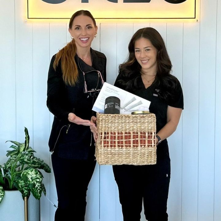 Two women in black uniforms holding a gift basket in front of a white wall and potted plant