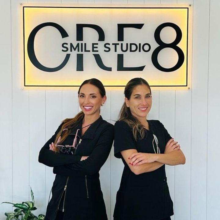 Two women posing in front of a lit CR8 Smile Studio sign