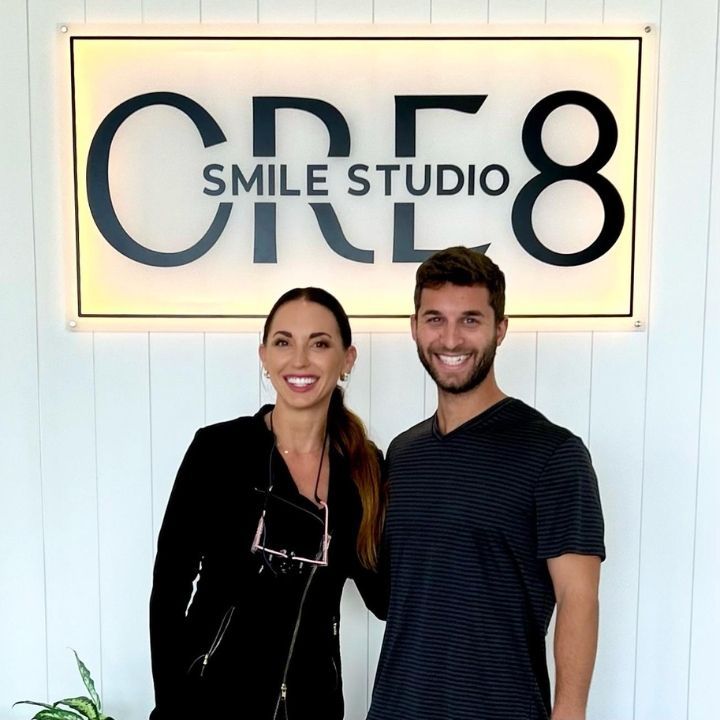 Two people smiling in front of a CERE8 Smile Studio sign