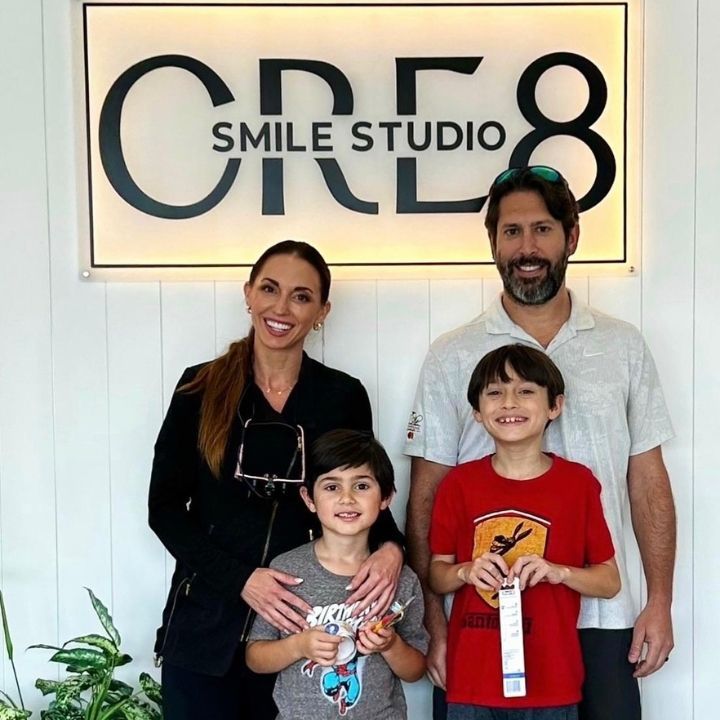 Four people smiling in front of a CRE8 Smile Studio sign, two children holding items.