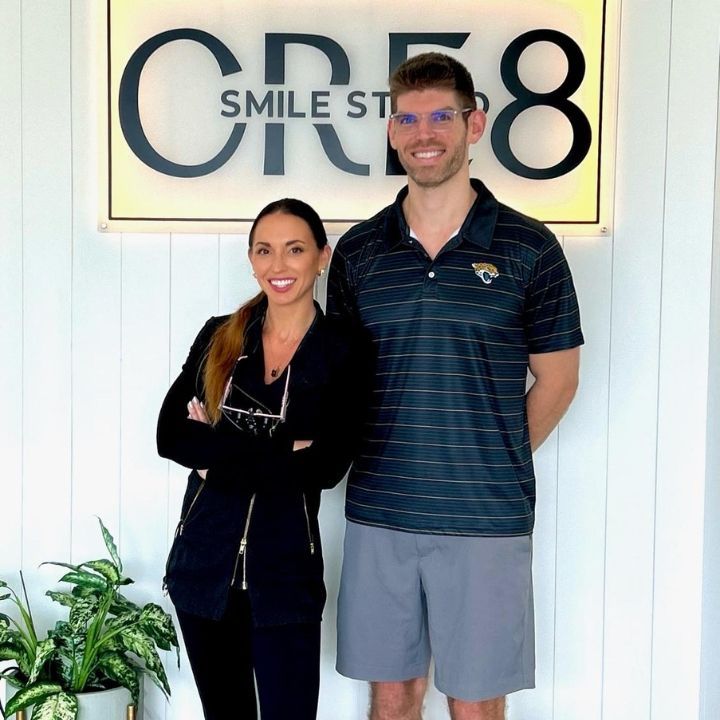 Two people standing in front of a CRES Smile Studio sign, smiling indoors.