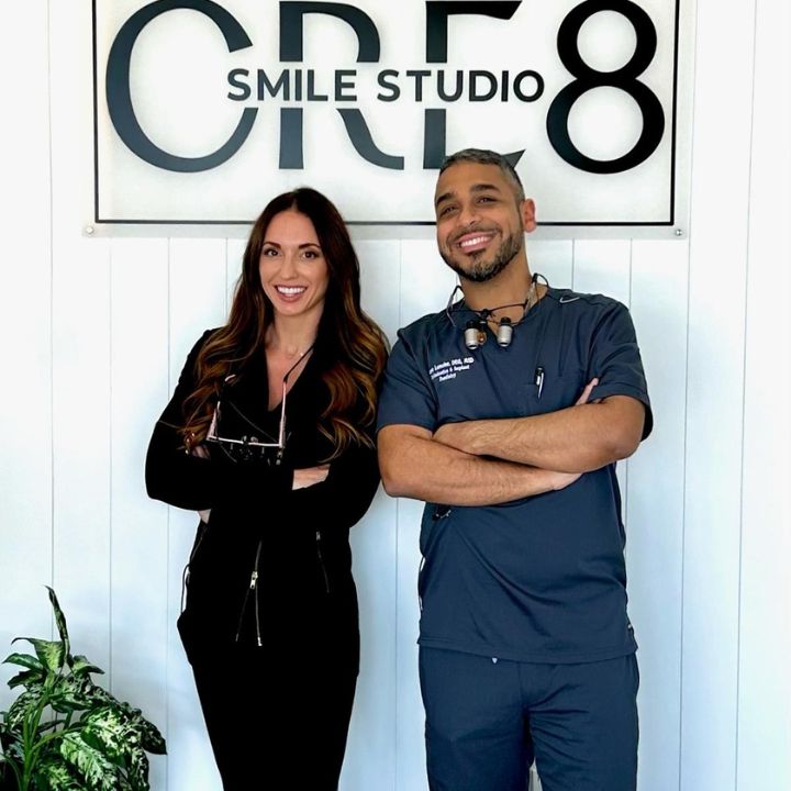 Two people standing in front of a C8 Smile Studio sign, arms crossed and smiling.