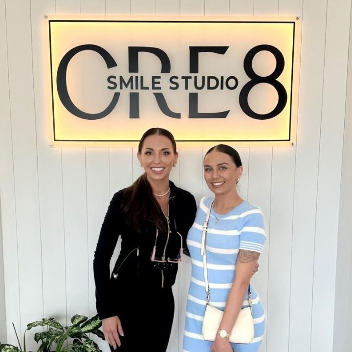 Two women standing in front of a lit sign reading “SMILE STUDIO CRE8”