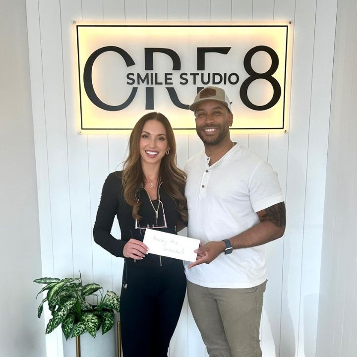 Two people smiling and holding a check in front of a Smile Studio 8 sign