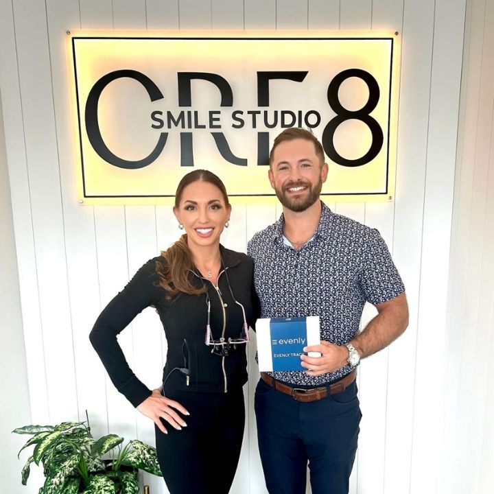 Two people standing in front of a glowing CRES Smile Studio sign, holding a book and smiling