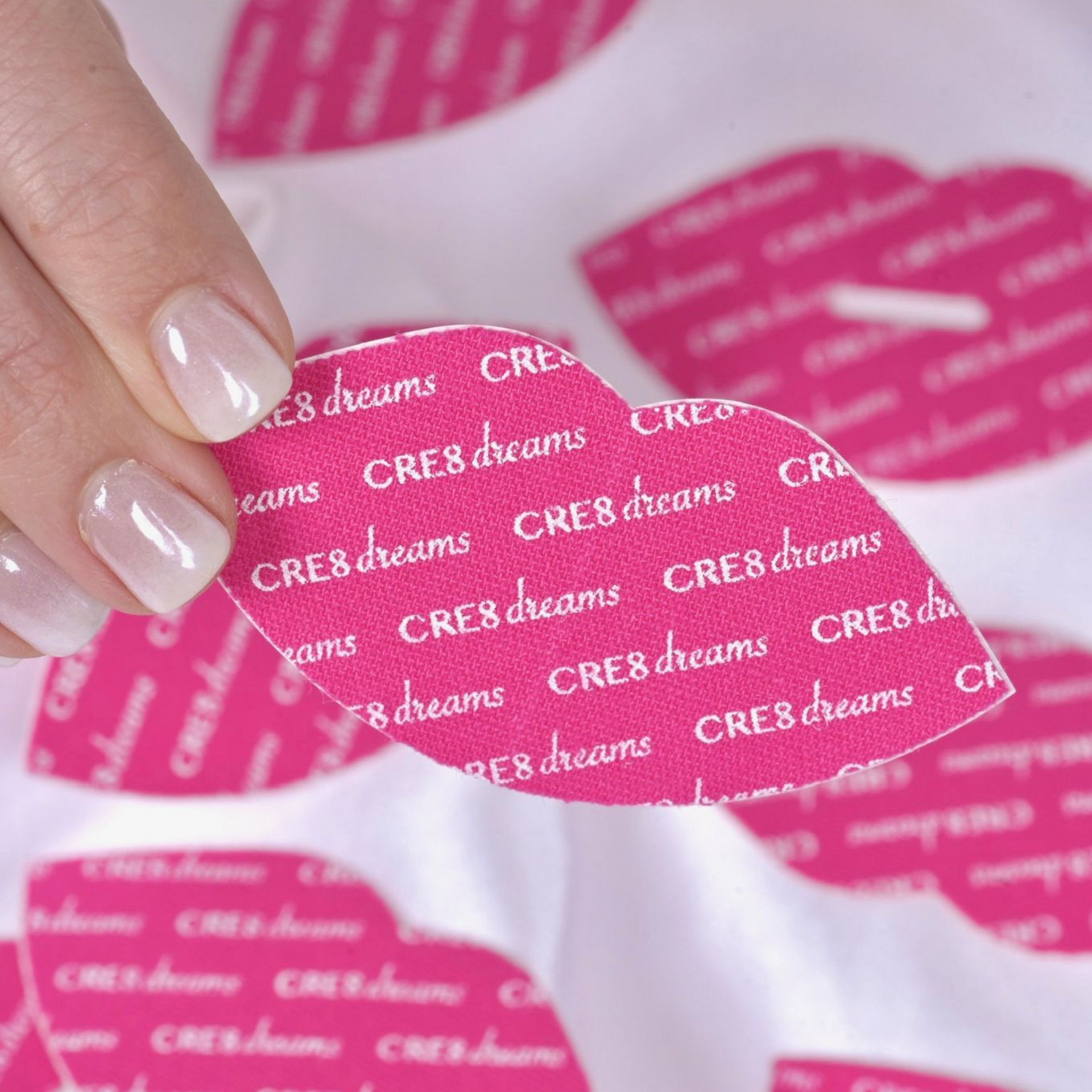 Pink CRE8 dreams logo stickers on a woman’s manicured nails in a close-up beauty shot