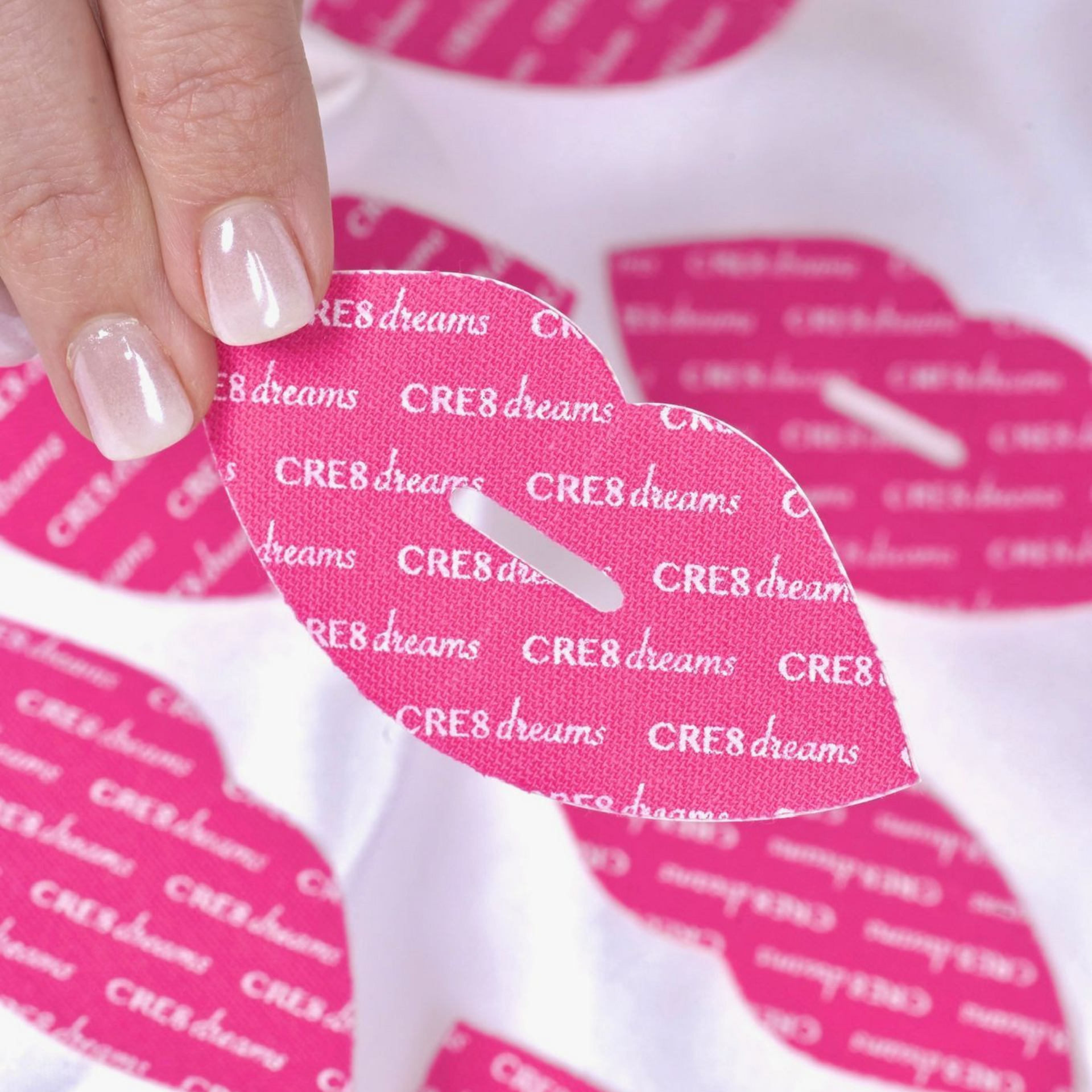 Hand holding a pink and white patterned fabric with repeated CRE8dreams text