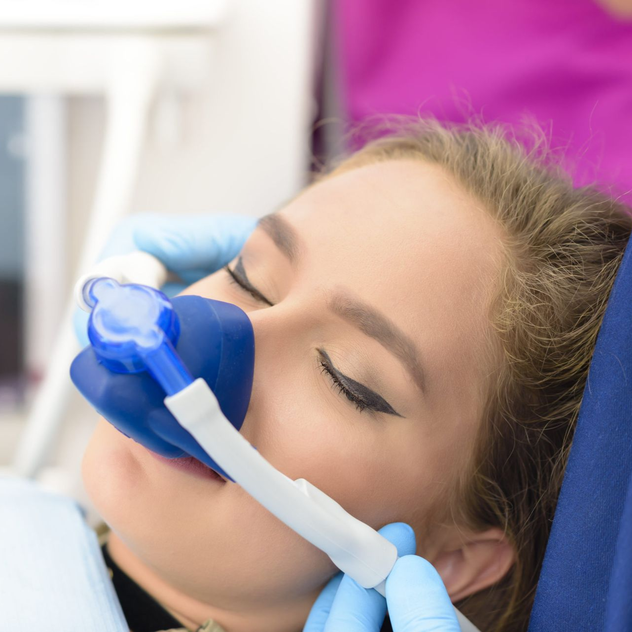 Patient receiving a facial treatment with a blue mask and tubing, eyes closed, in a spa setting