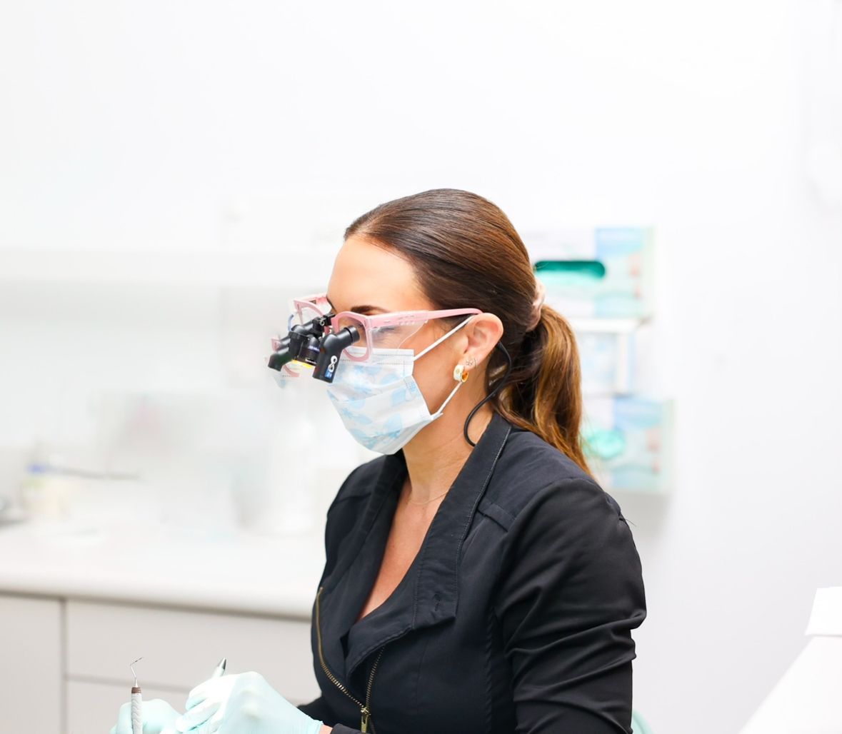 Dentist wearing a face mask and magnifying loupes in a bright clinic, looking to the right