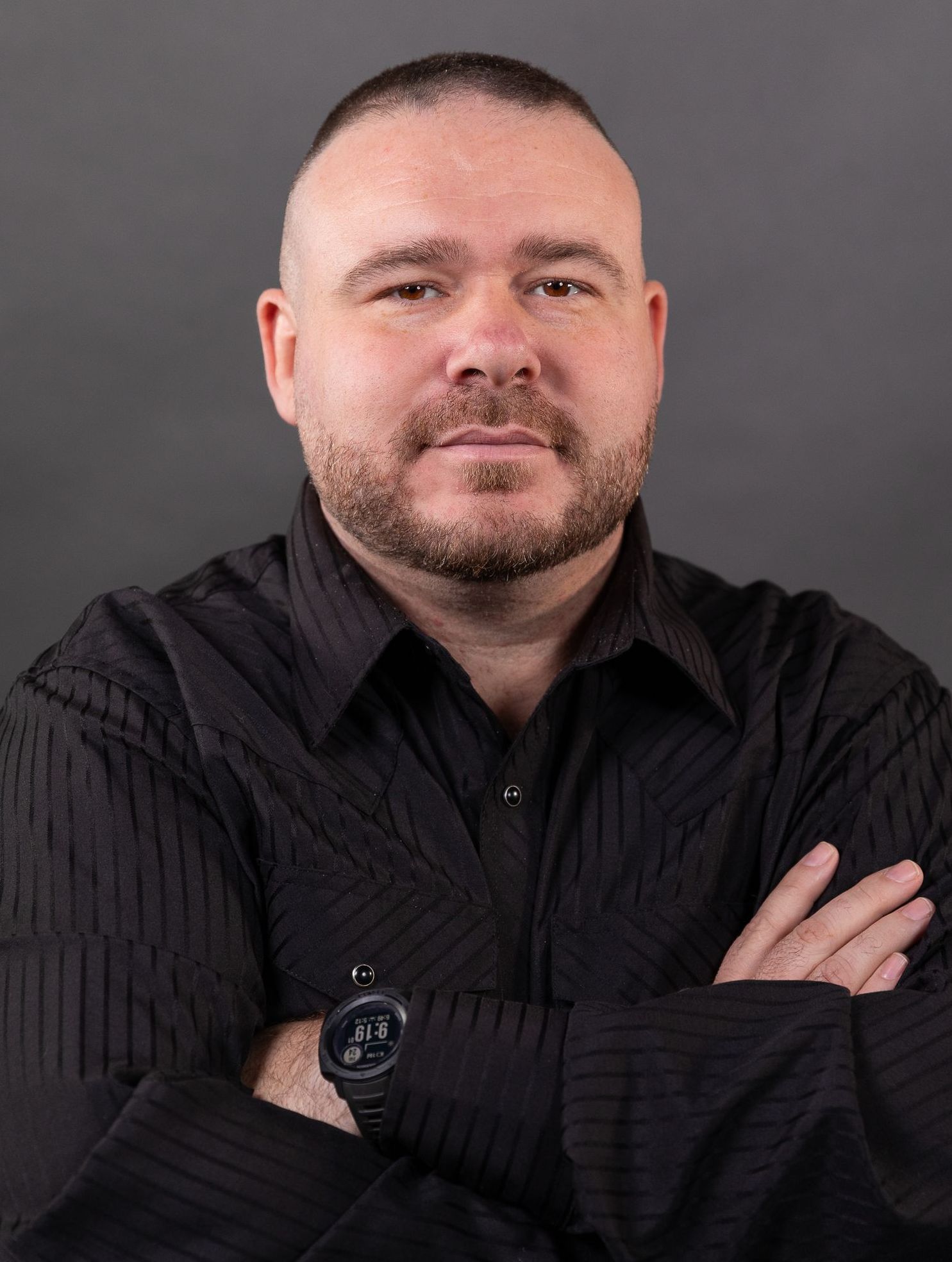 A man with a beard is wearing a black shirt and a watch.