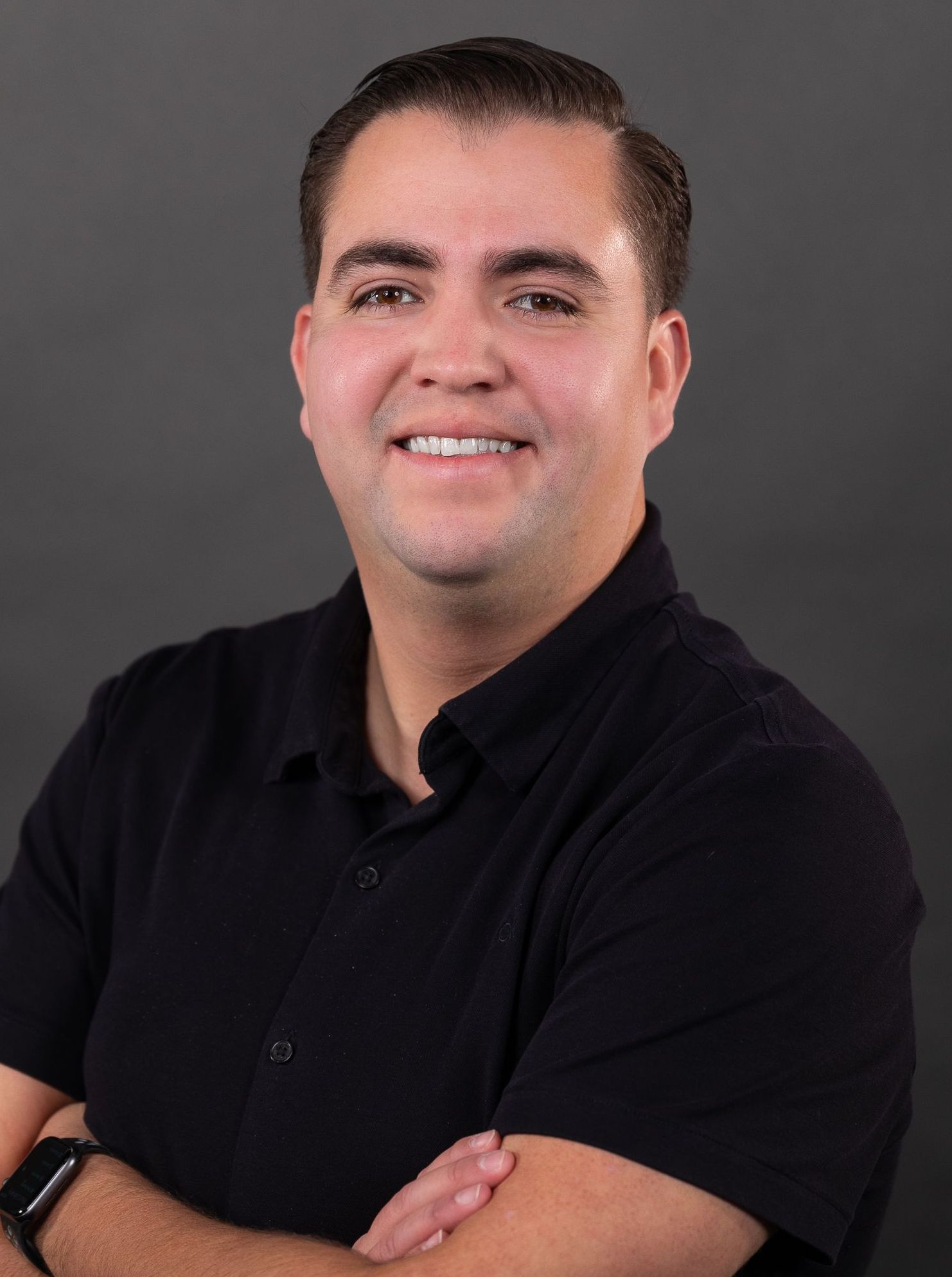 A man in a black shirt is smiling with his arms crossed.