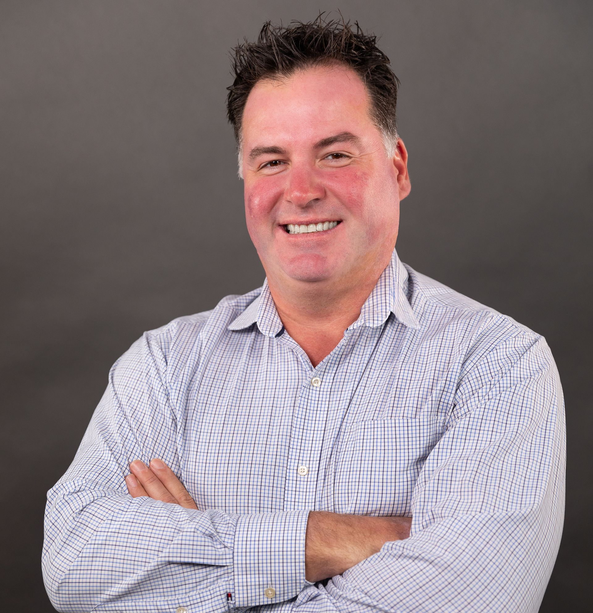 A man in a plaid shirt is smiling with his arms crossed.