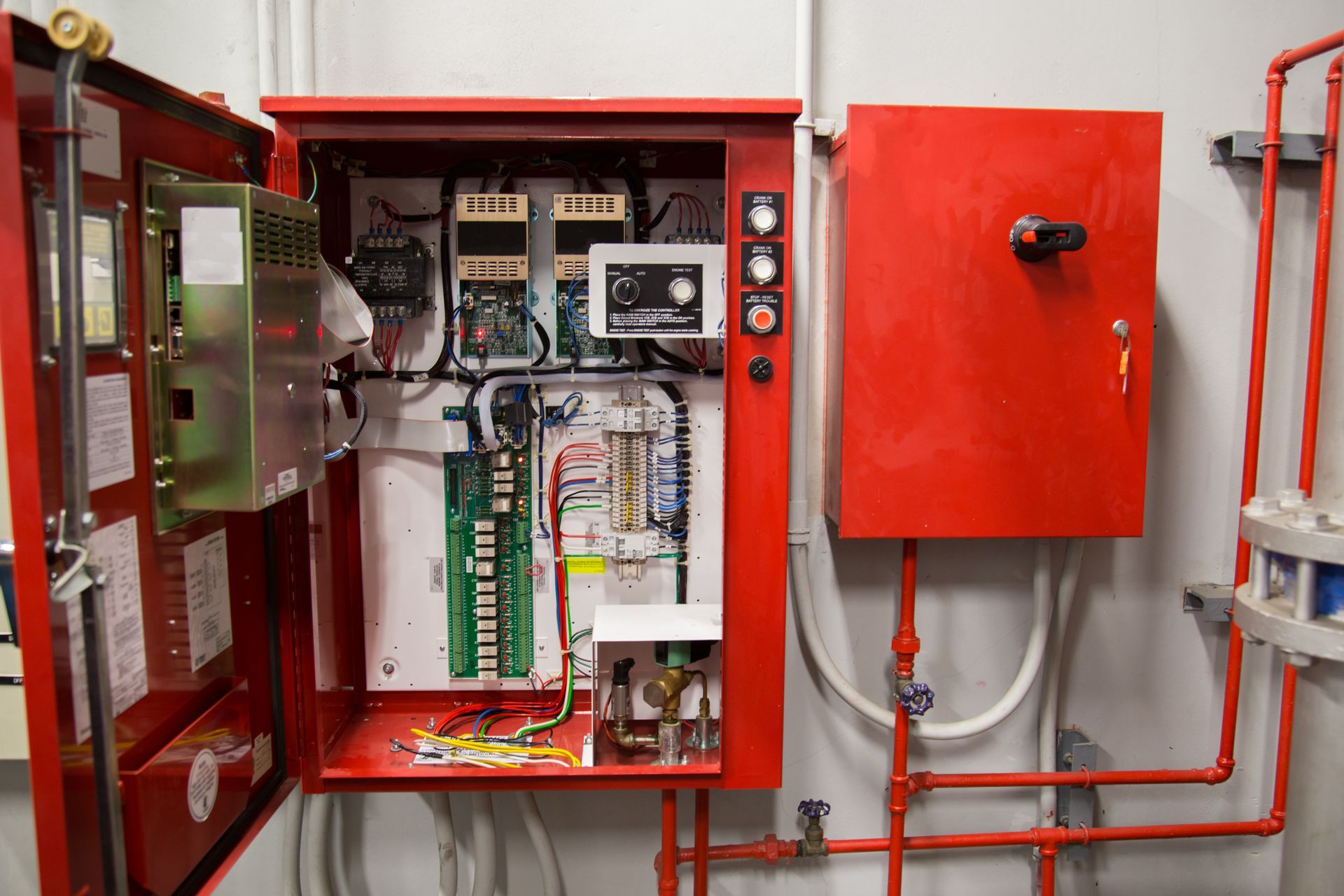 Open electrical control panel with wiring and gauges mounted on a white wall in a utility room
