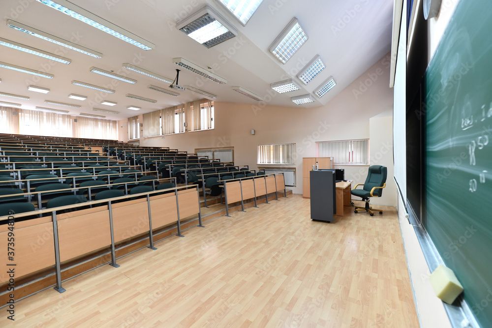 An empty lecture hall with rows of chairs and a blackboard.