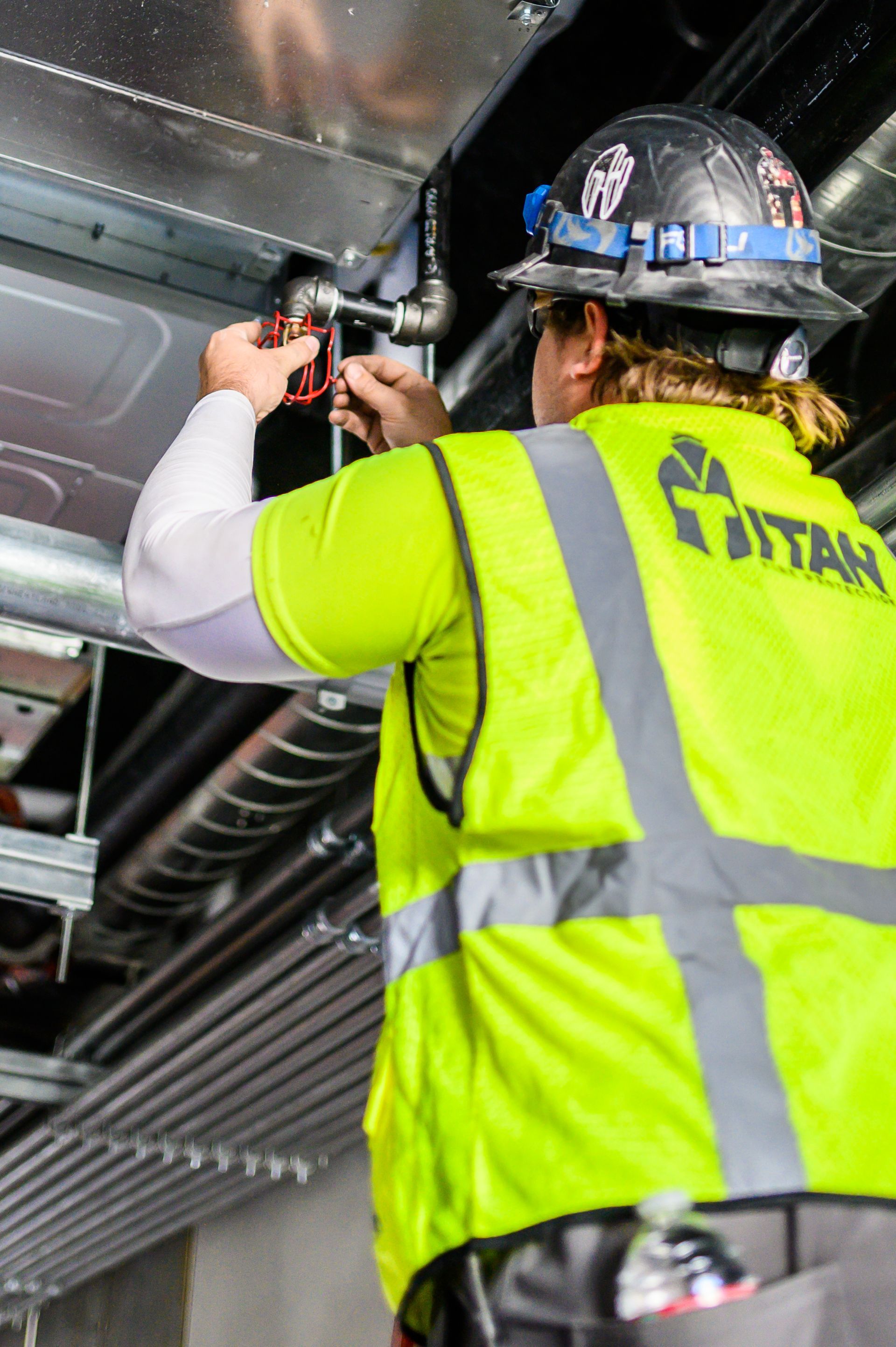 Construction worker in a neon vest, working on overhead pipes inside a building.