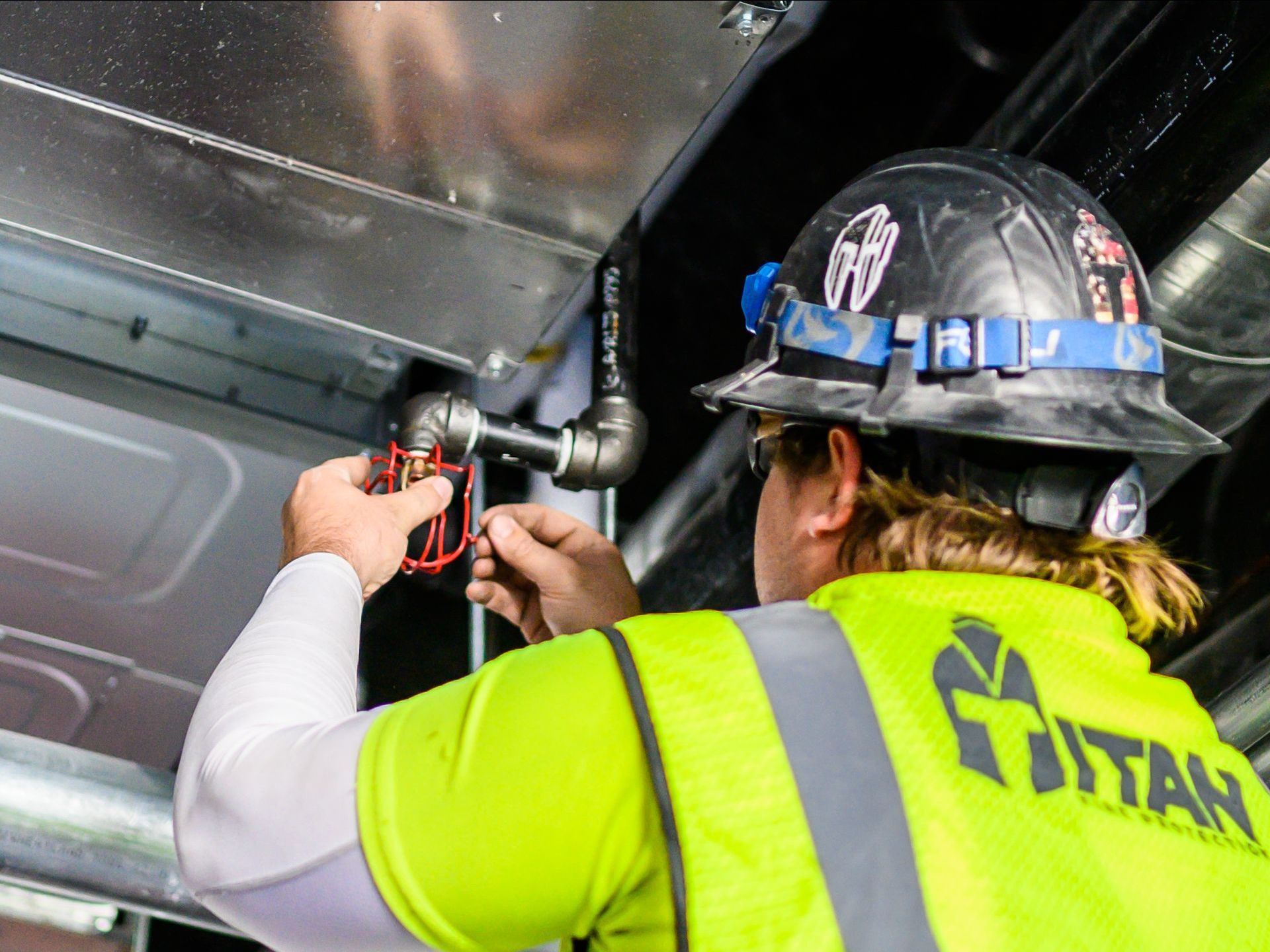 Worker in hard hat and safety vest adjusting wiring inside metal equipment panel