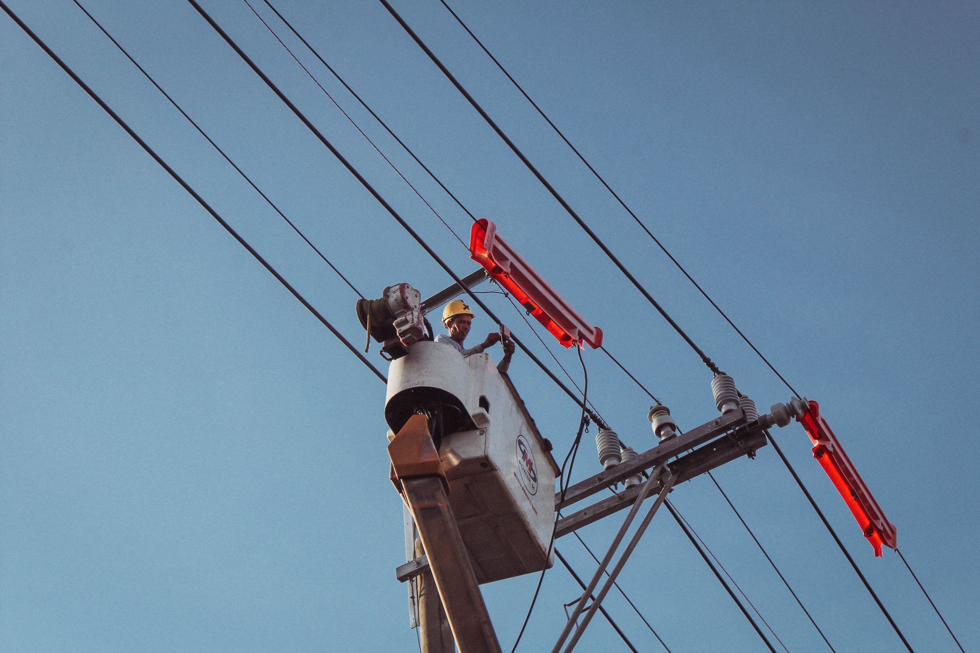 Utility worker in a bucket truck repairing power lines against a blue sky