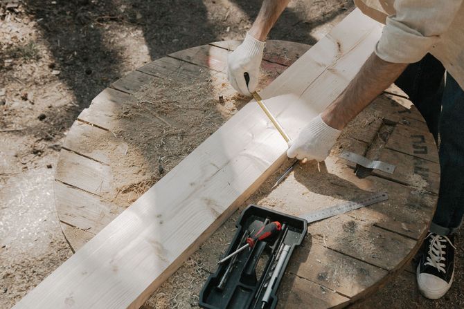 People measuring a white board outdoors beside a toolbox and tiles