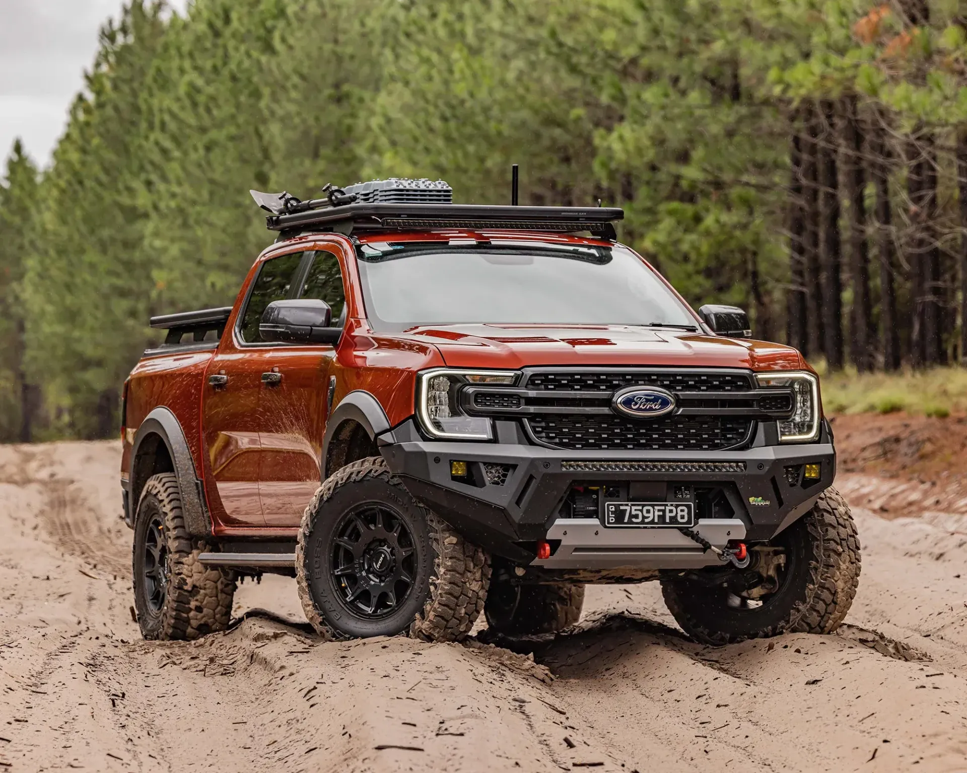 Orange off-road pickup truck on a sandy trail in a pine forest, with roof rack and mud tires. — Whitsunday 4x4 & Automotive In Proserpine, QLD