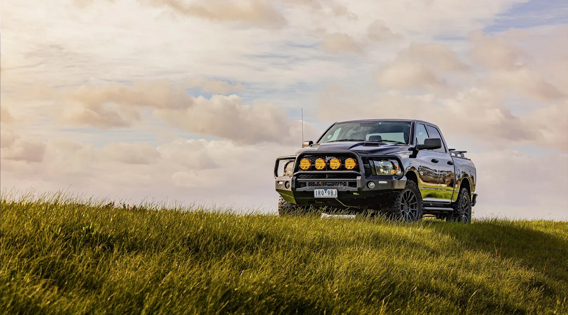Black off-road truck on grassy hill under a cloudy sky — Whitsunday 4x4 & Automotive In Proserpine, QLD