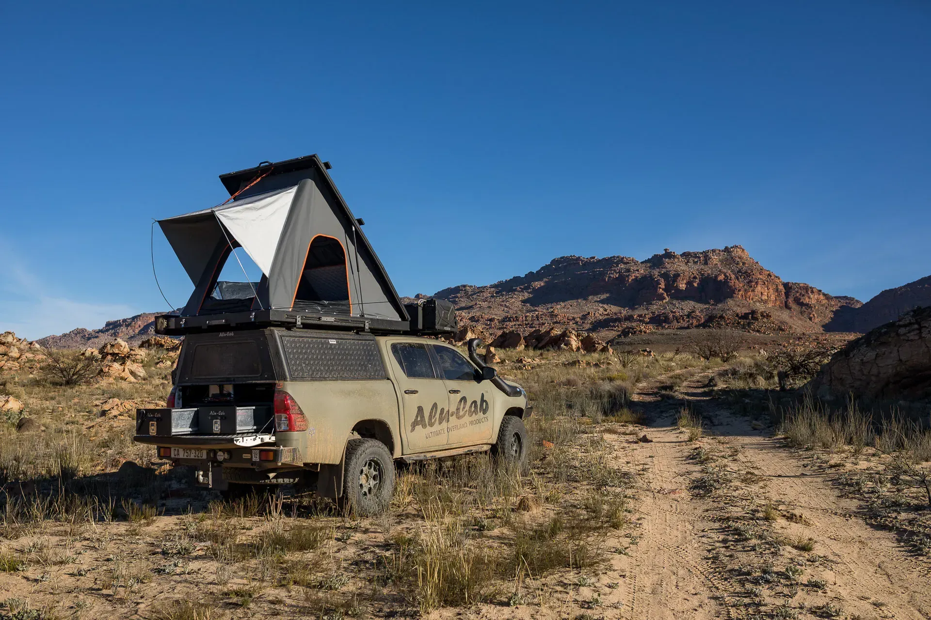 Off-road camper van with rooftop tent parked on a desert trail beside rocky hills under a blue sky — Whitsunday 4x4 & Automotive In Proserpine, QLD