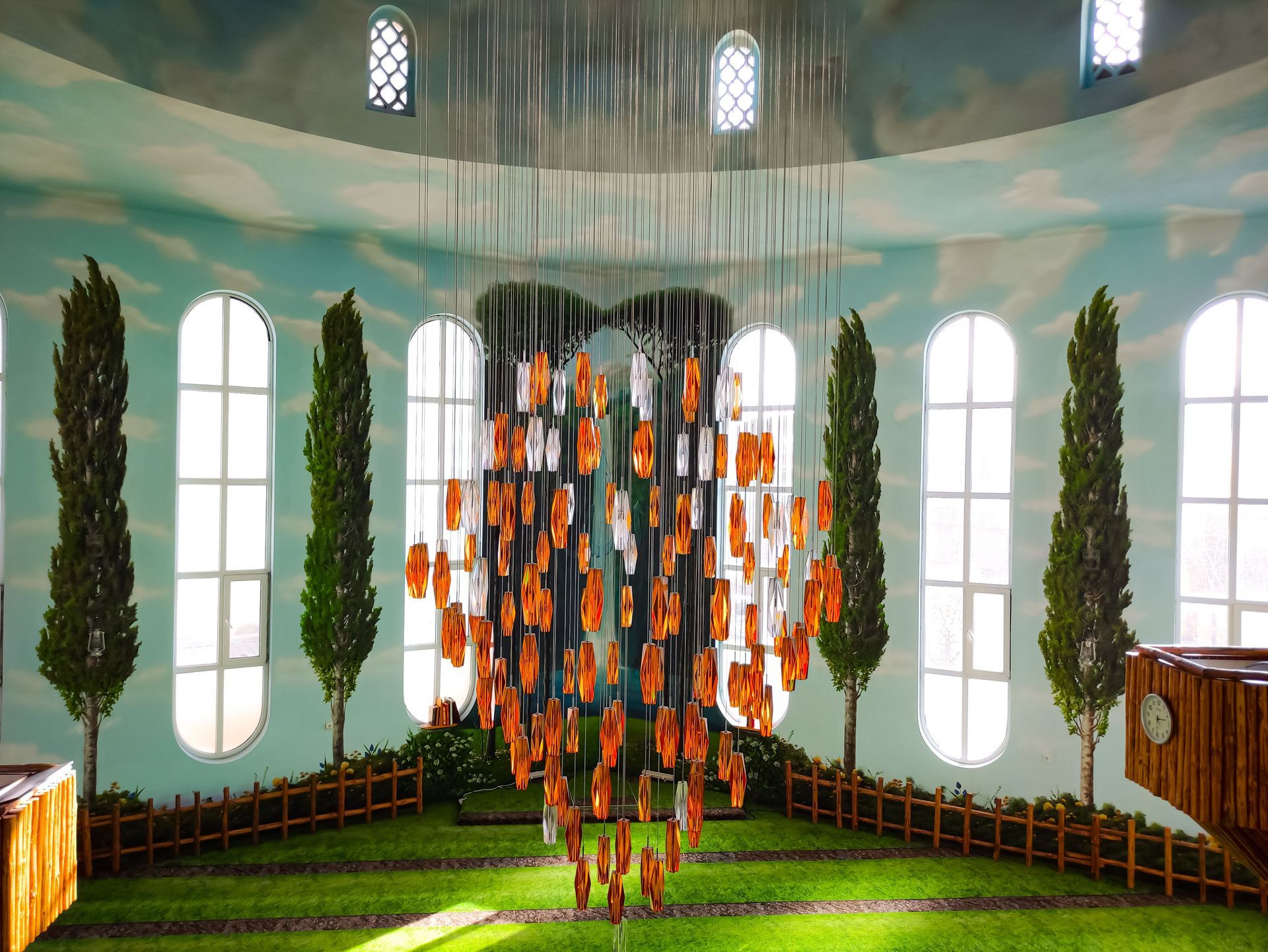 Hanging orange lantern sculpture in a bright circular room with tall windows and green walls