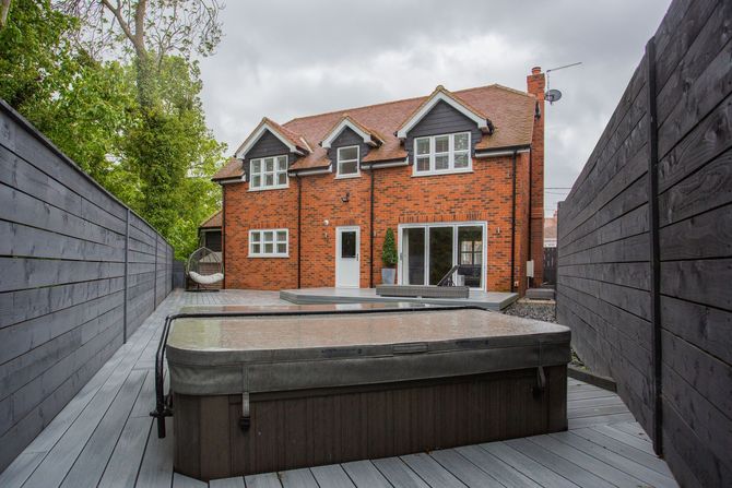 Backyard patio with hot tub facing a red brick house and gray deck fencing