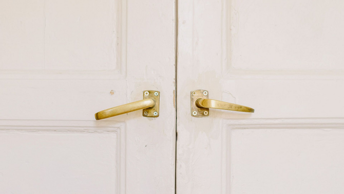 White double doors with gold handles and locks, closed in a plain interior setting