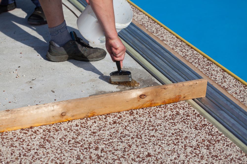 Person applying coating to a rooftop edge with a brush next to gravel and metal flashing