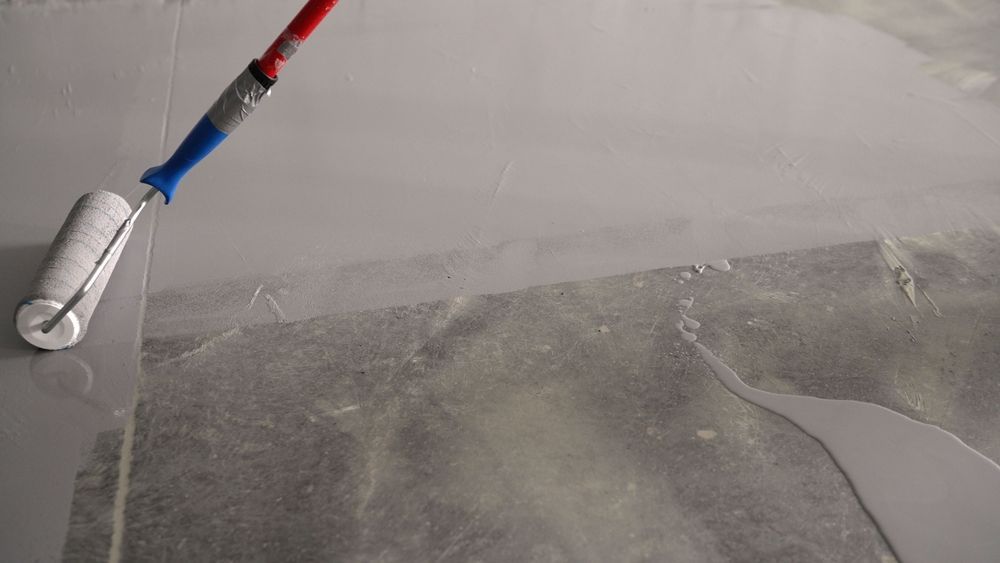Paint roller applying gray paint to a wall corner, creating a smooth patch on a textured surface.
