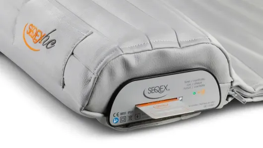Gray portable cushion-like medical device with a control panel and orange accent branding