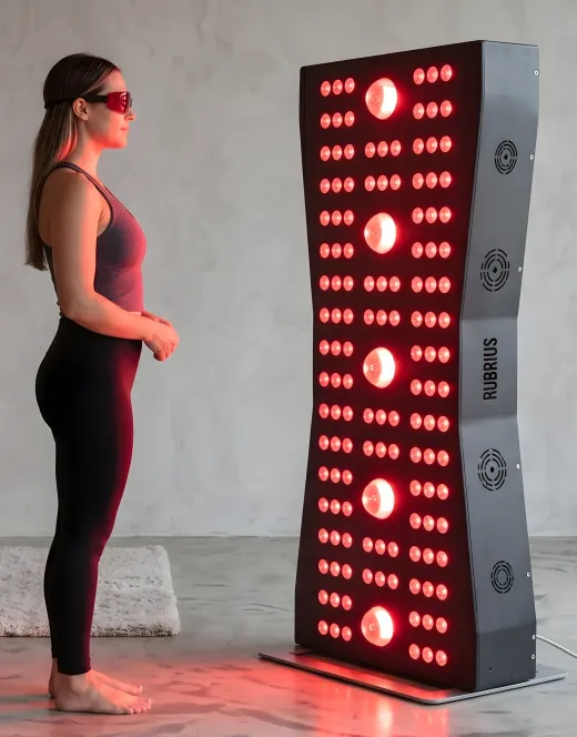 Woman standing beside a glowing red light therapy panel in a studio room