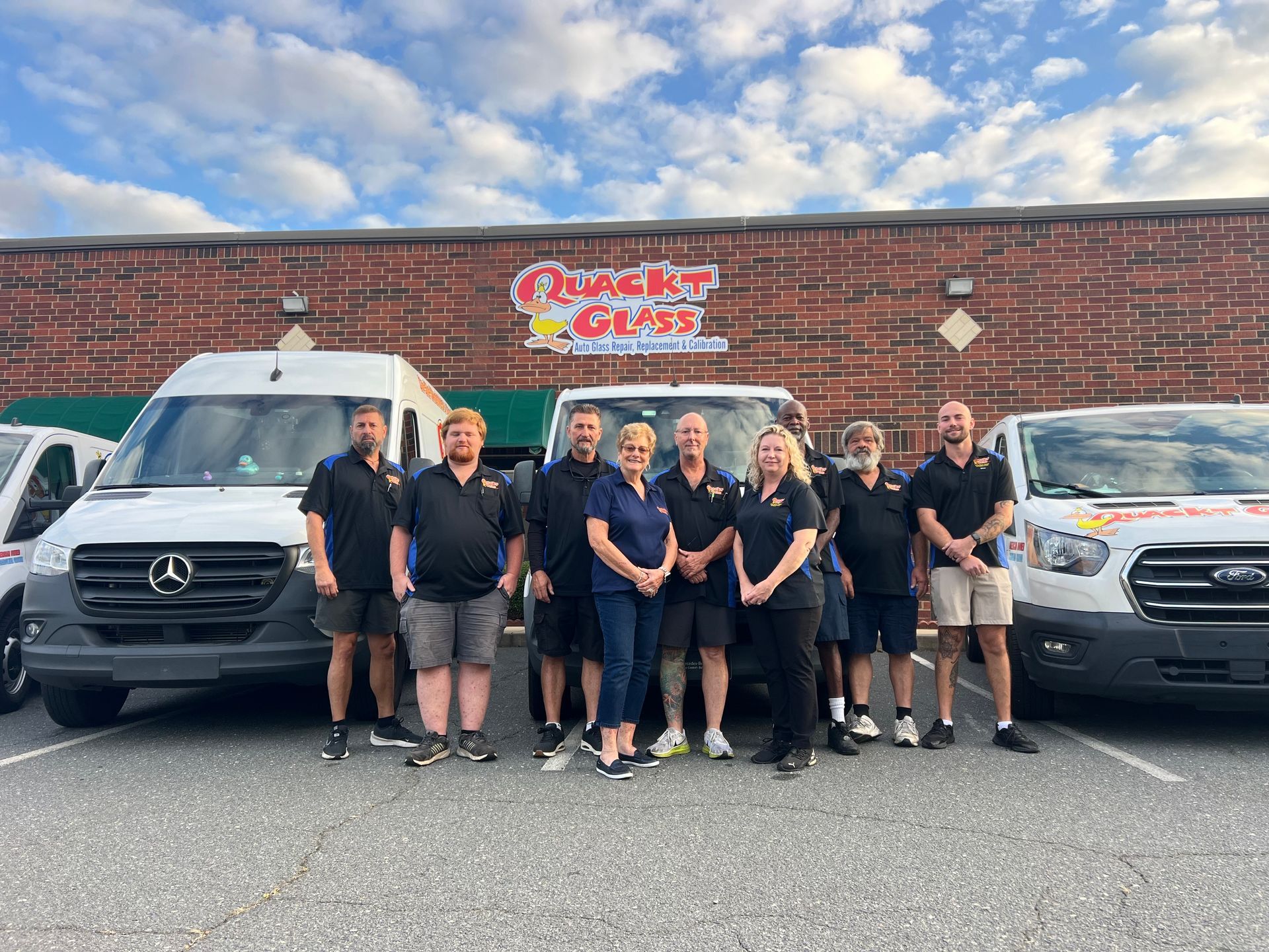 Group of people standing in front of vans with a business sign.