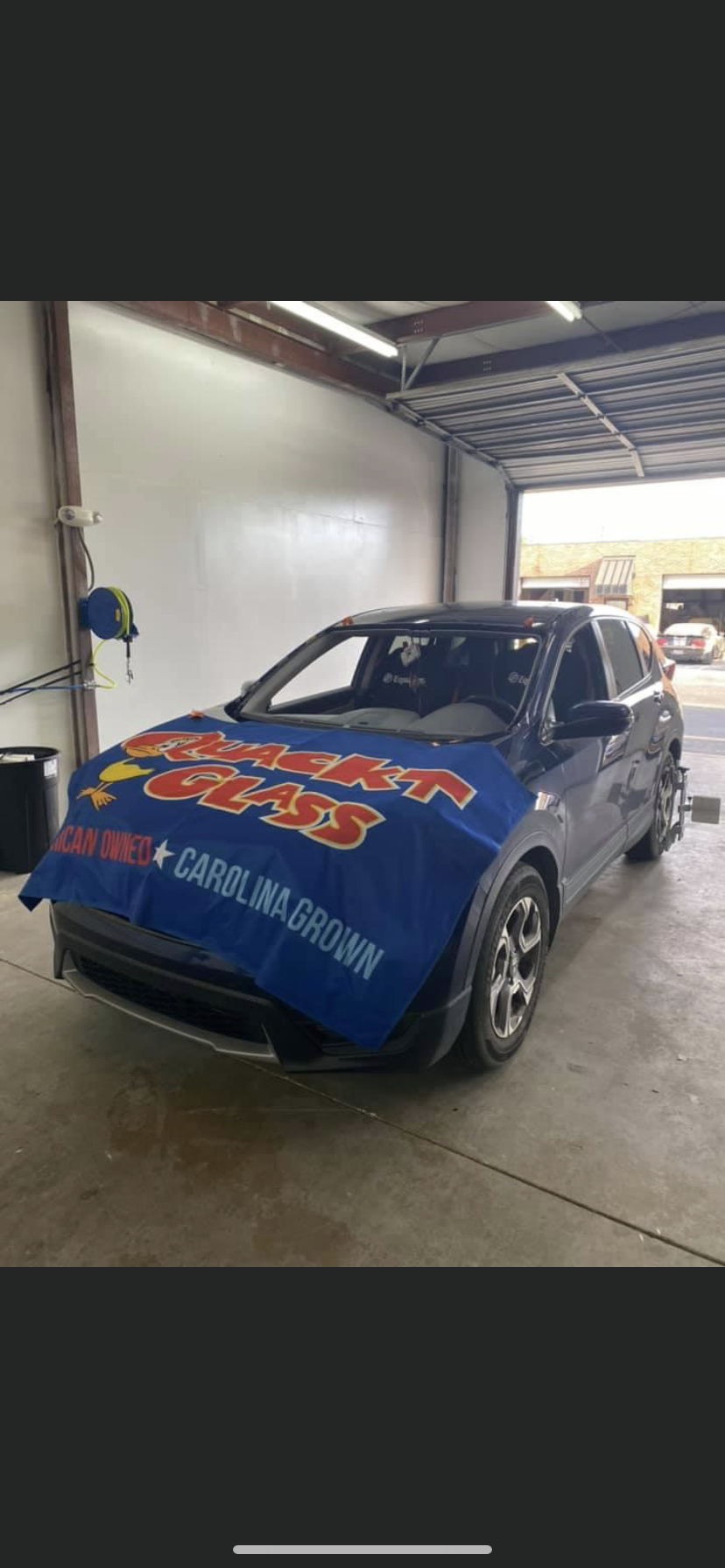 A dark blue car in a garage covered with a blue protective cover, likely for repairs.