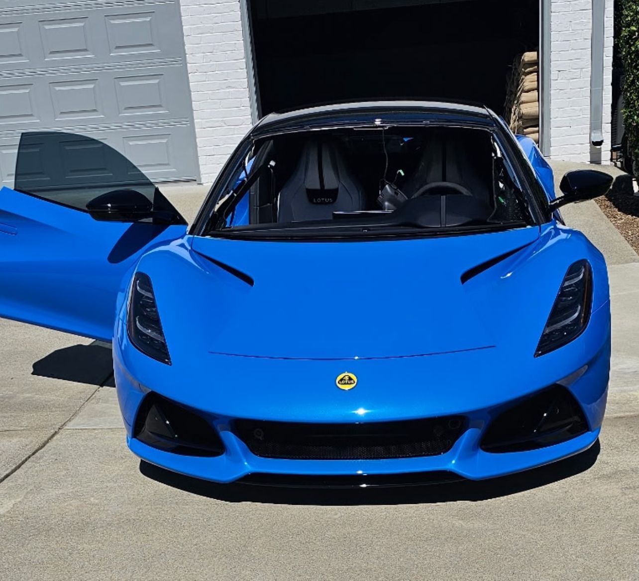 Blue sports car with door open, parked in front of a garage.
