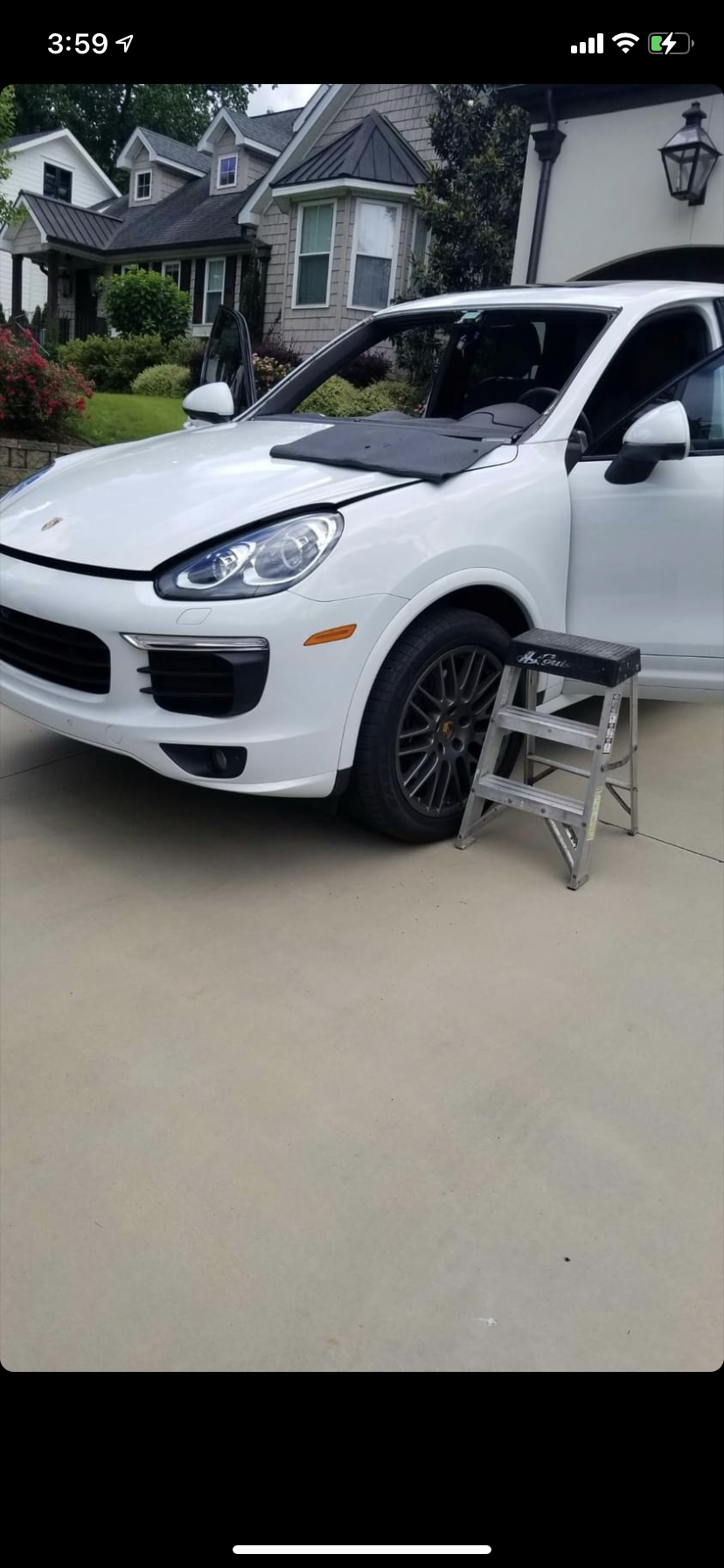A white Porsche Cayenne with the door open, a step stool next to it, parked in a driveway.