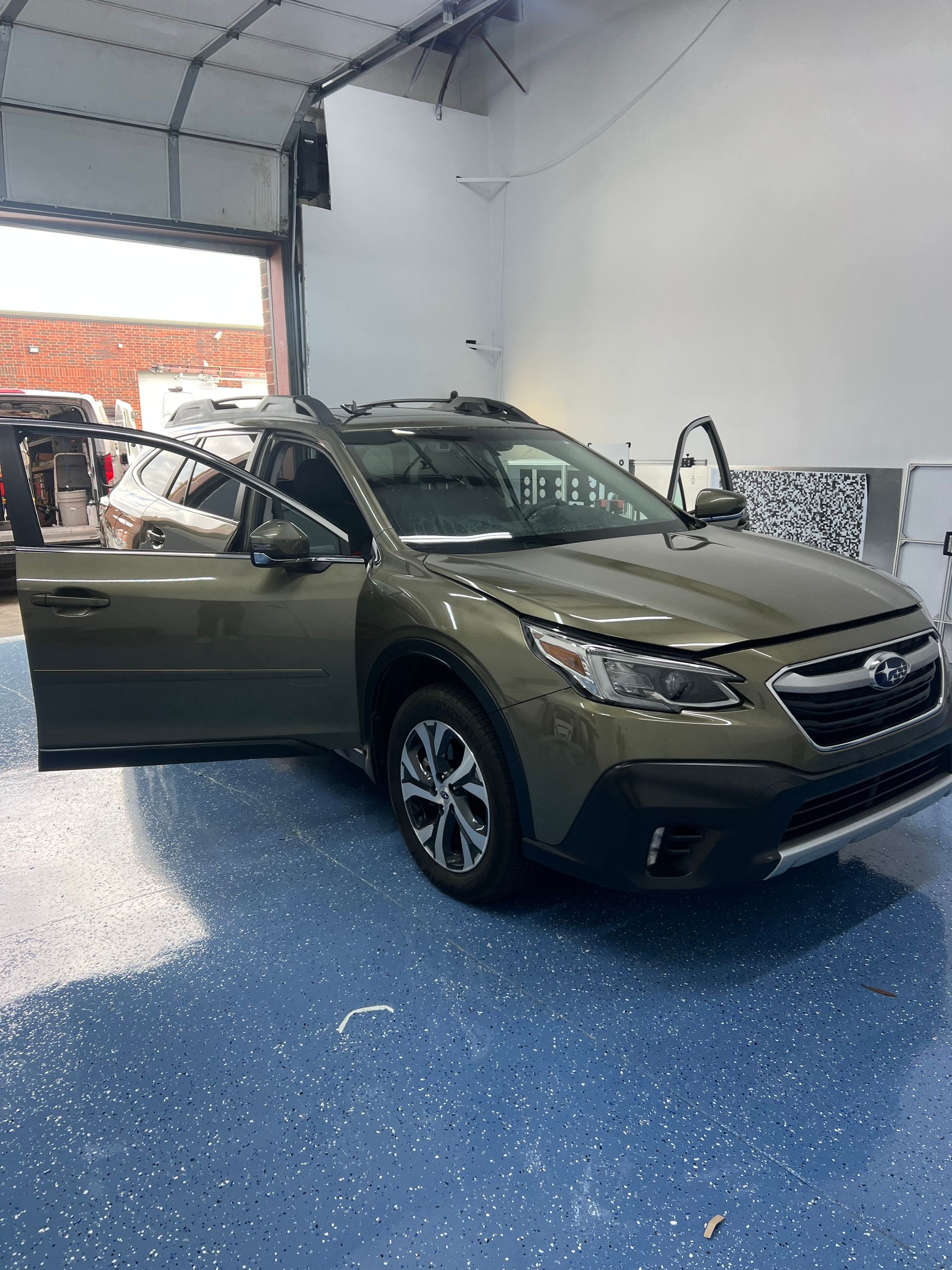 Green Subaru Outback with doors open inside a garage with blue speckled floor.