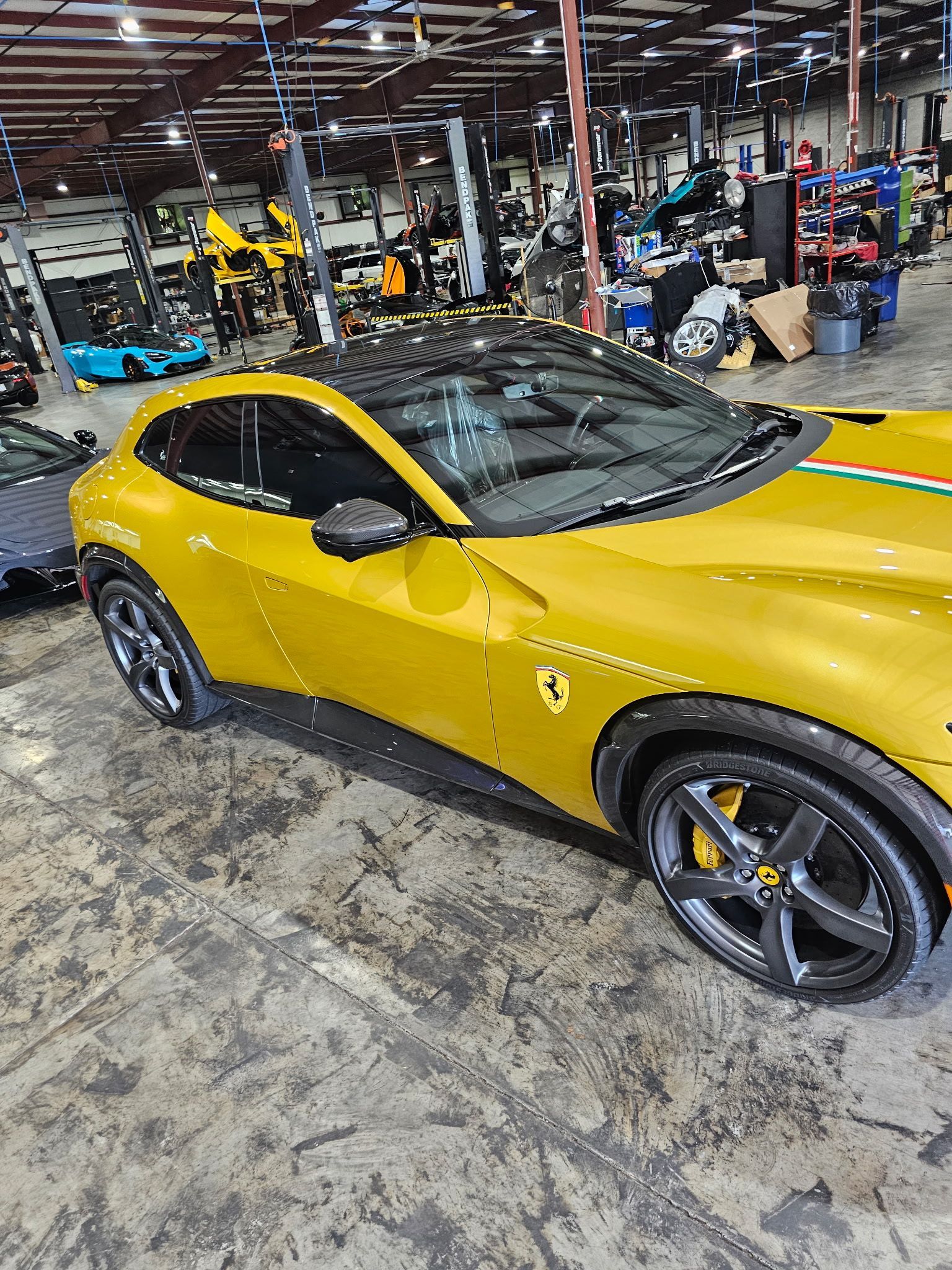 Yellow Ferrari with black roof and wheels in a cluttered warehouse setting.