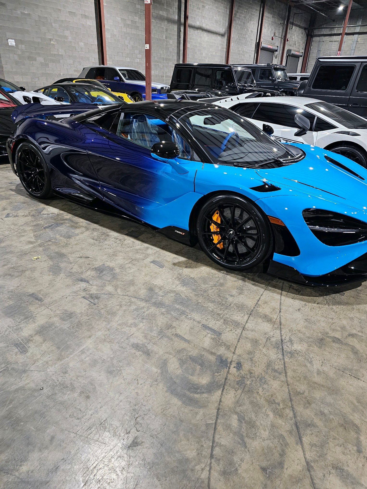 Blue and black McLaren sports car parked in a garage with other vehicles.