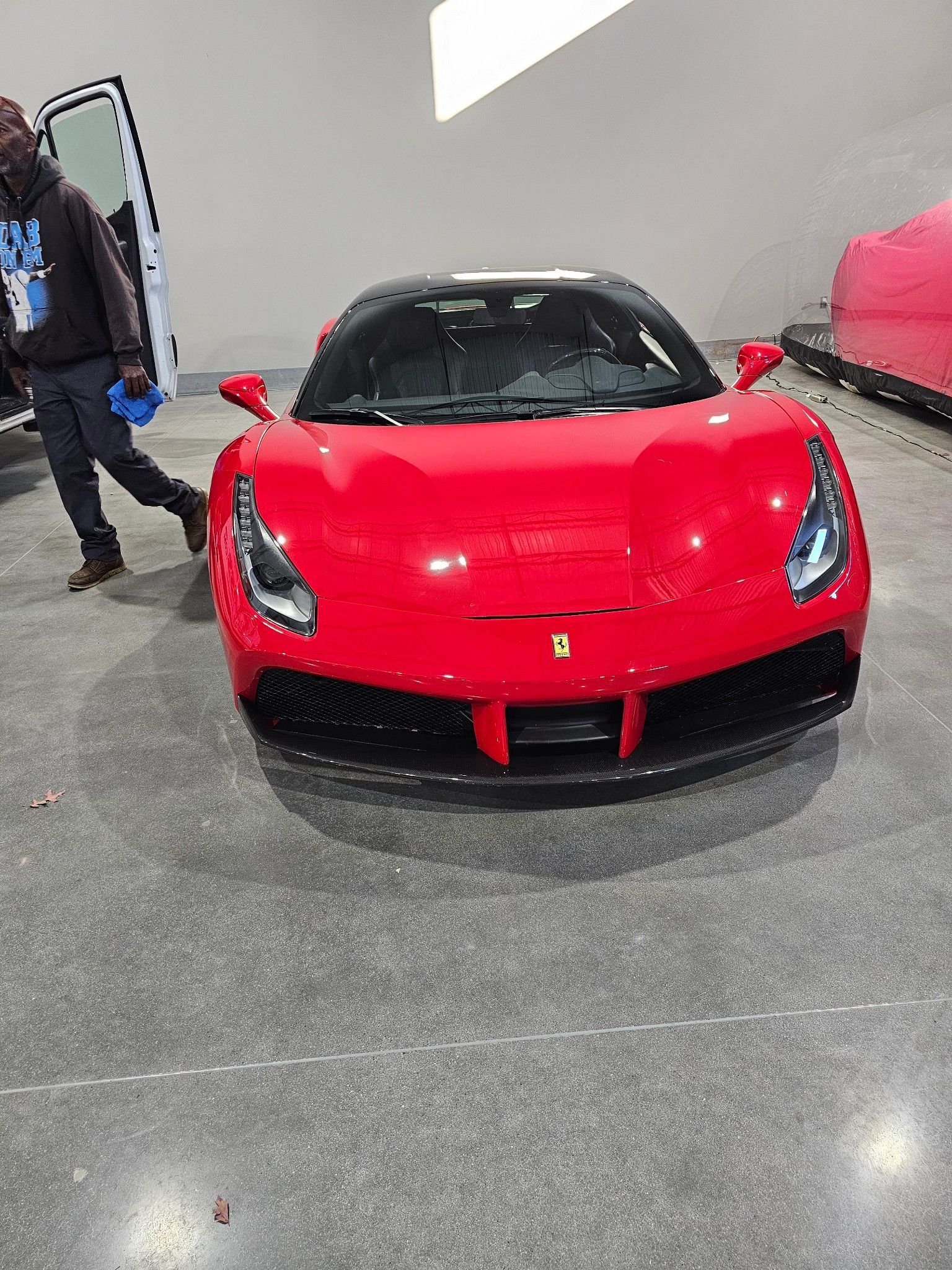Red Ferrari sports car with black roof, parked in a showroom; a person is standing by the open door.