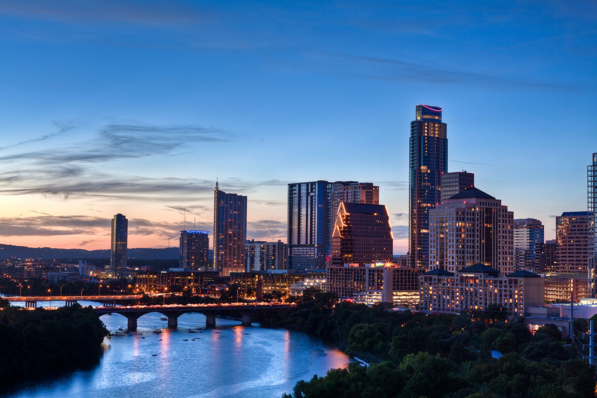 Austin, Texas skyline along Lady Bird Lake at dusk with lit skyscrapers reflecting in the water.