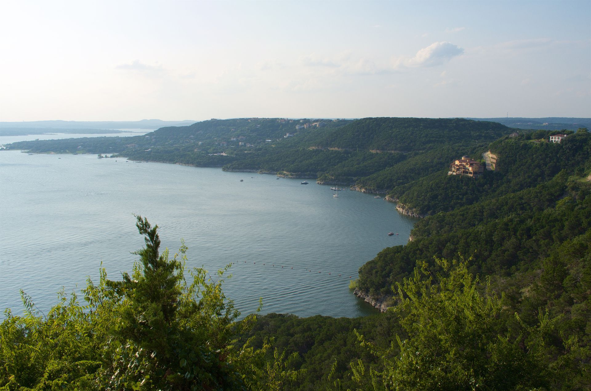 A wide-angle view of a lake bordered by dense, forested hills under a clear sky.